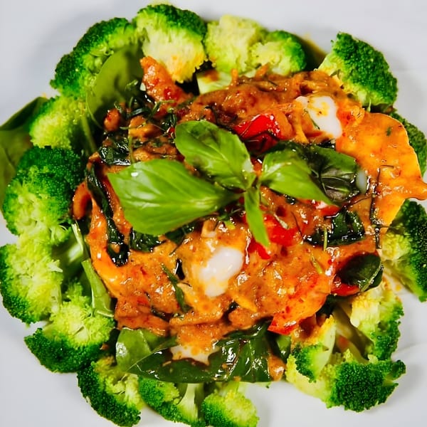Asian-fusion dish with chicken, red curry sauce, basil, and broccoli florets on a white plate.