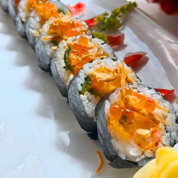 A close-up of a row of Phatt Pho n' Sushi rolls, topped with bright orange roe and crispy elements.