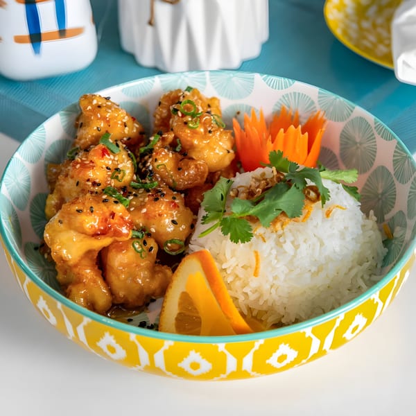 Phatt Pho n' Sushi's orange chicken with rice, garnished with cilantro, sesame seeds, and orange slices.