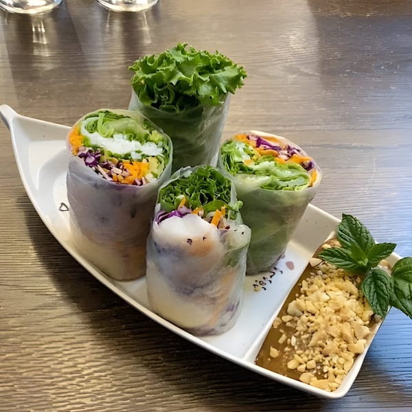 Four fresh spring rolls with colorful vegetables and herbs, served with peanut sauce and mint.
