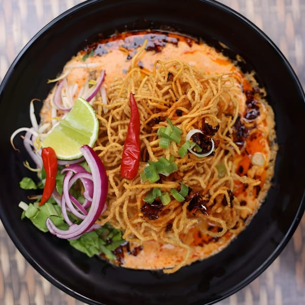 Phatt Pho n' Sushi's Khao Soi with crispy noodles, red chili, lime, and red onion.