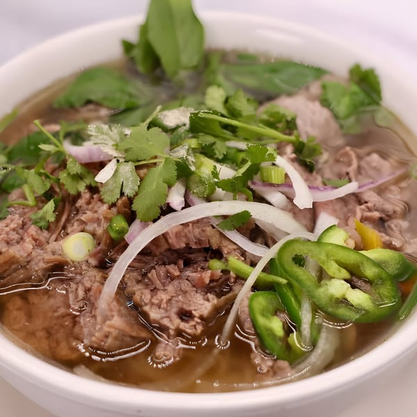 Close-up of a bowl of Phatt Pho n' Sushi's pho, topped with beef, onions, cilantro, and green peppers.
